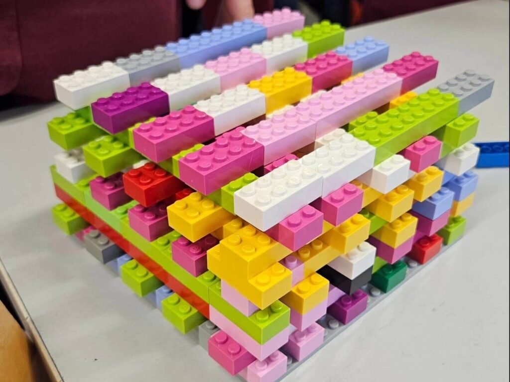 Layered LEGO brick structure built from overlapping rows of multicolour blocks on a table.