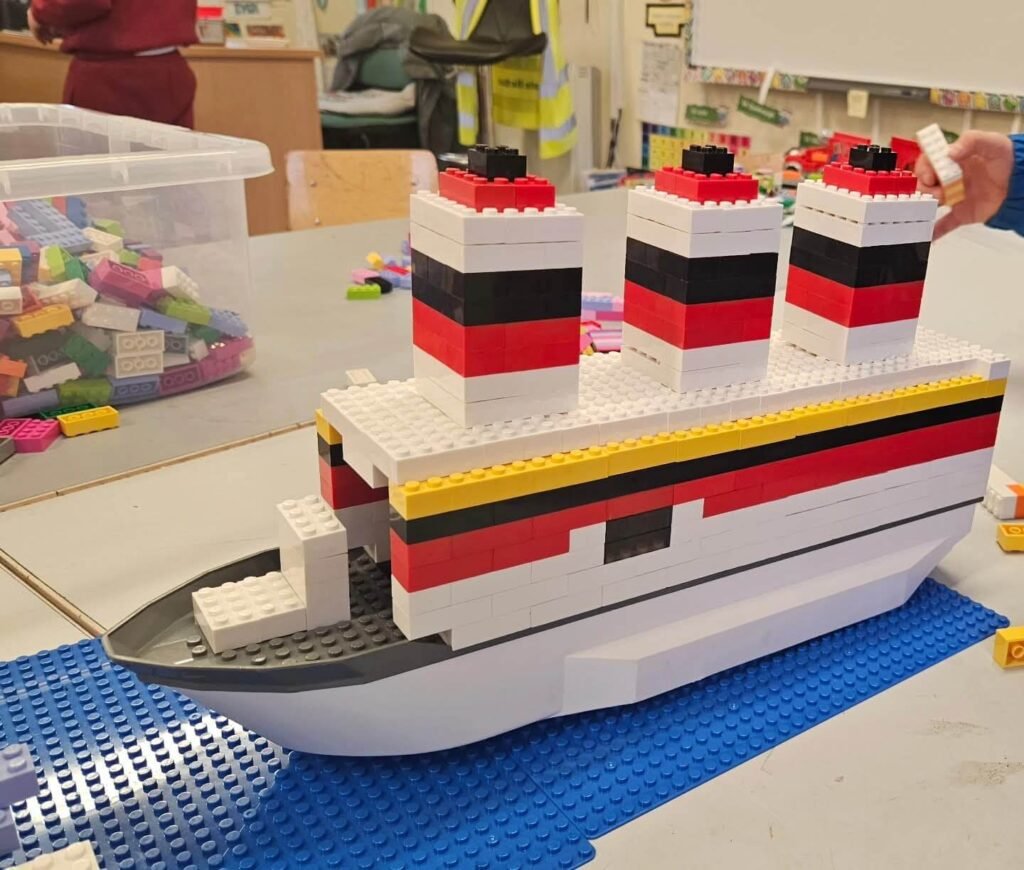 LEGO ship model built from white, red, and black bricks, displayed on blue baseplates.