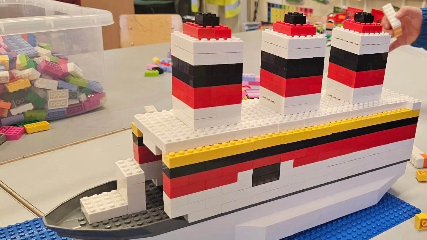 LEGO ship model built from white, red, and black bricks, displayed on blue baseplates.