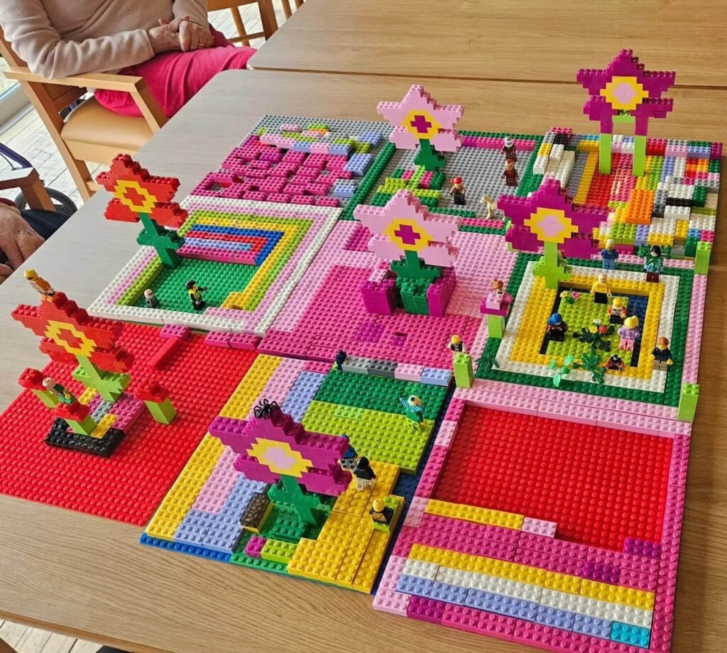 LEGO baseplates arranged with flower structures, pathways, and small figures in multiple colours.