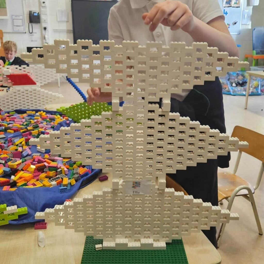 Tall LEGO structure built from white bricks with repeating openings, displayed on a baseplate in a classroom.