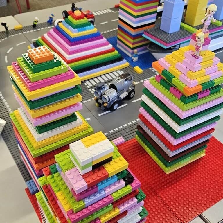 Colourful LEGO brick towers built from stacked square plates on a play mat with roads and small vehicles.